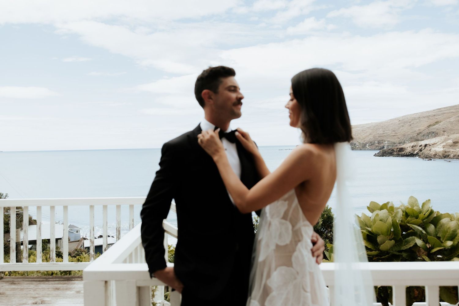 Elegant couple shares intimate moment on white balcony overlooking ocean view.