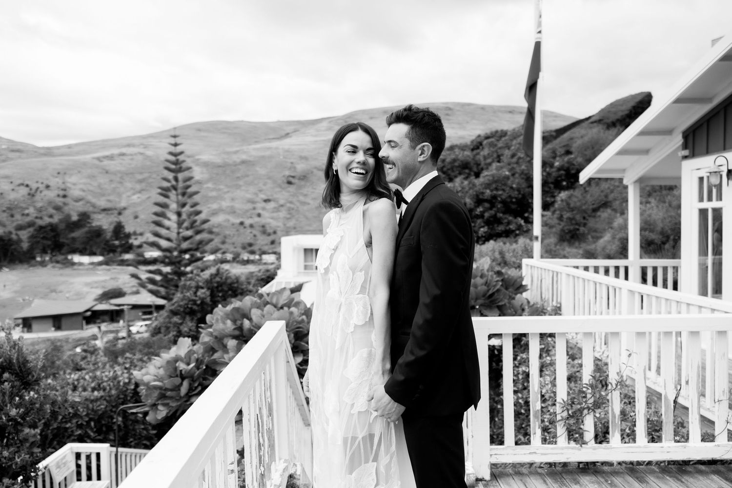 A couple shares an intimate moment along a white railed porch with mountain views.