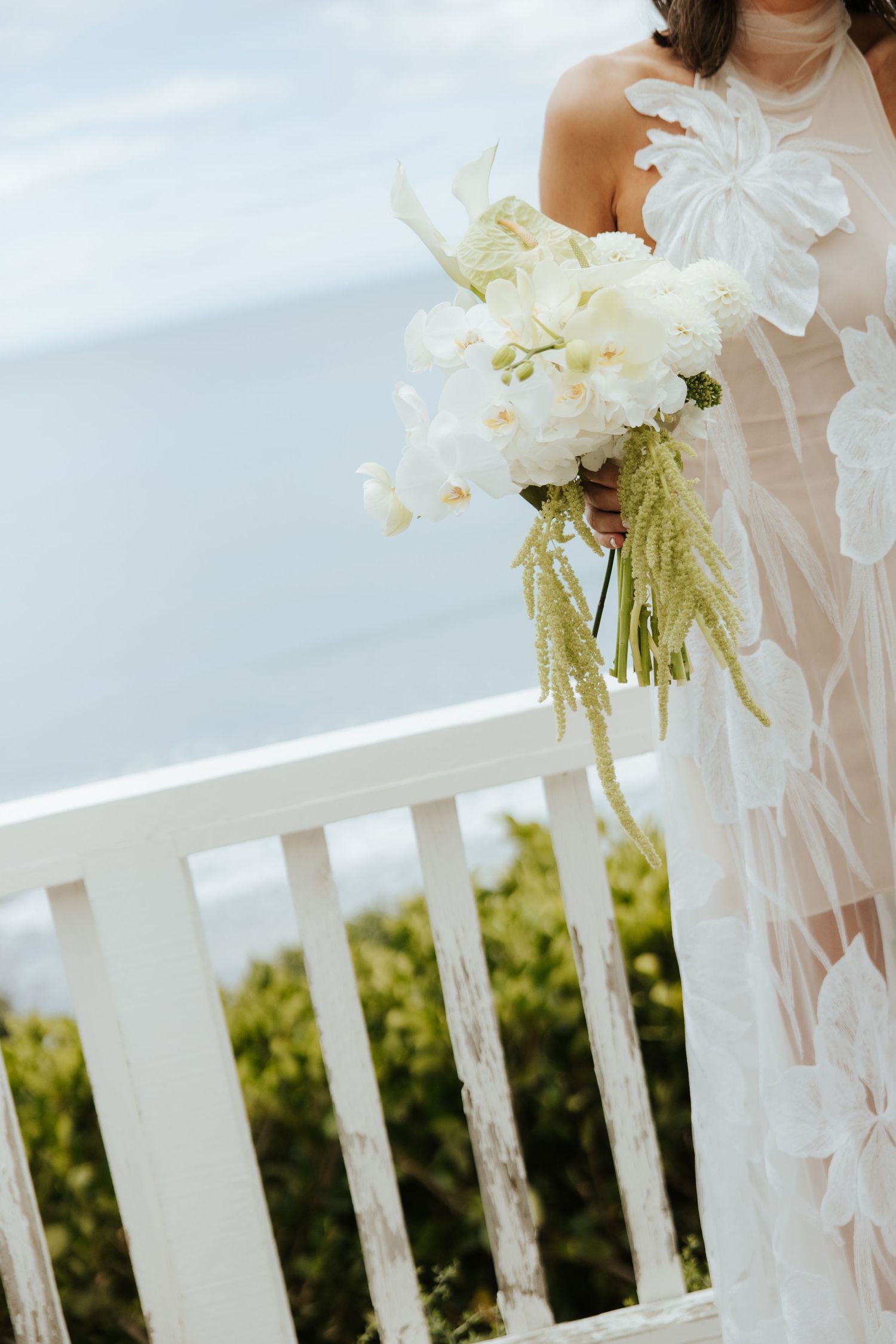 White floral wedding decorations adorn outdoor railing with greenery backdrop.