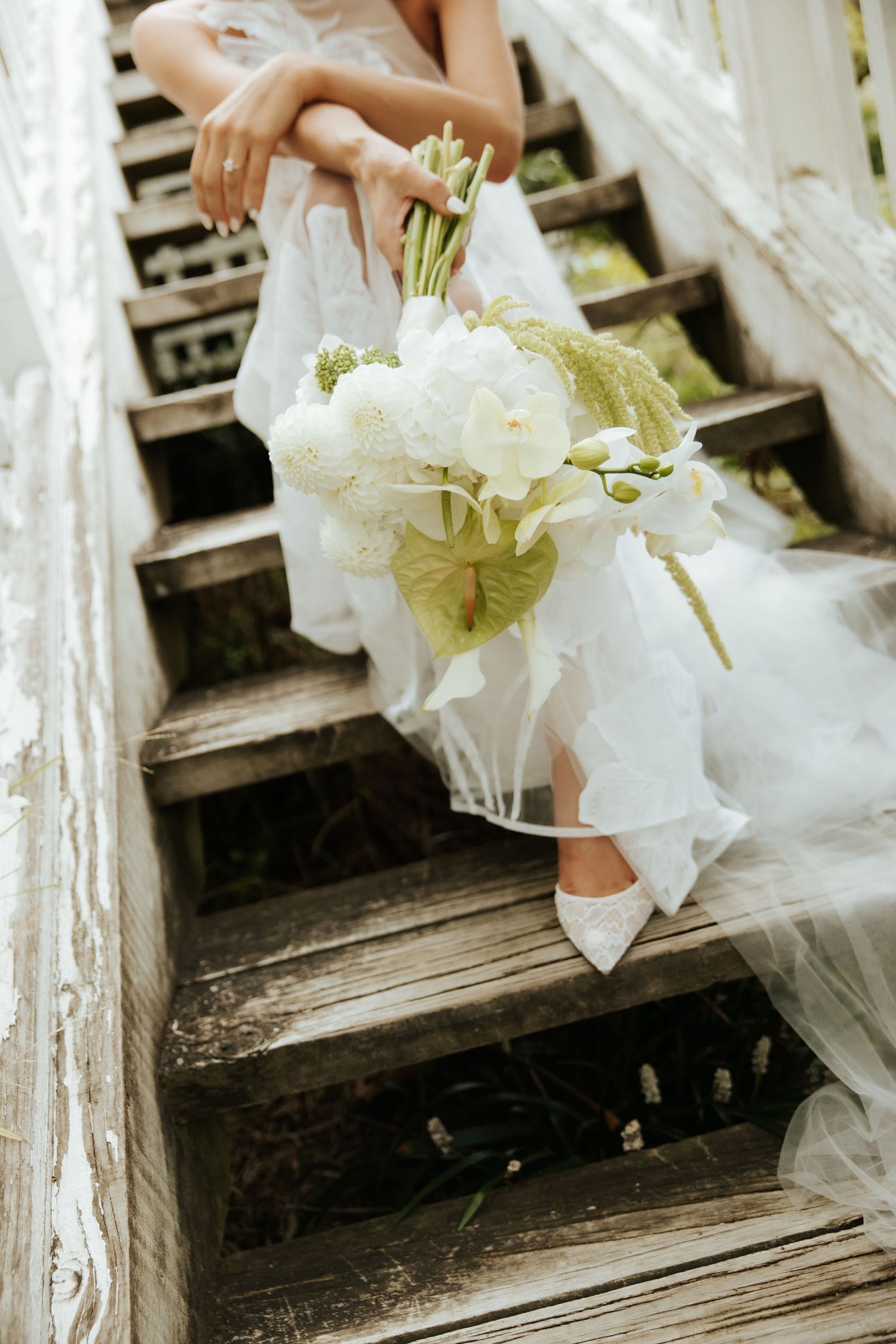 White bridal bouquet and dress detail on rustic wooden stairs.