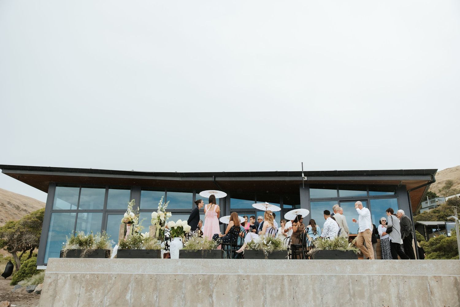 Modern glass venue with panoramic views hosts outdoor wedding celebration.