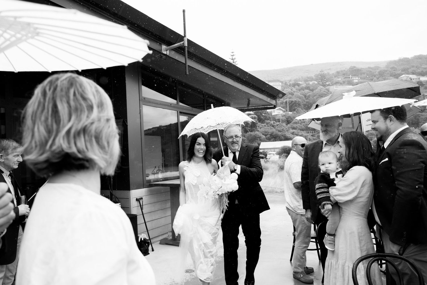 A wedding party gathering under umbrellas on a rainy day.