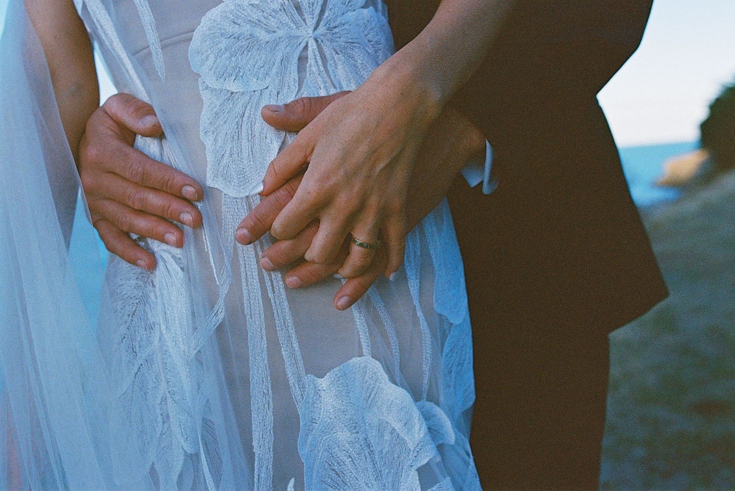 Close-up detail shots of a bride's white lace wedding dress with hands visible against a blurred background.