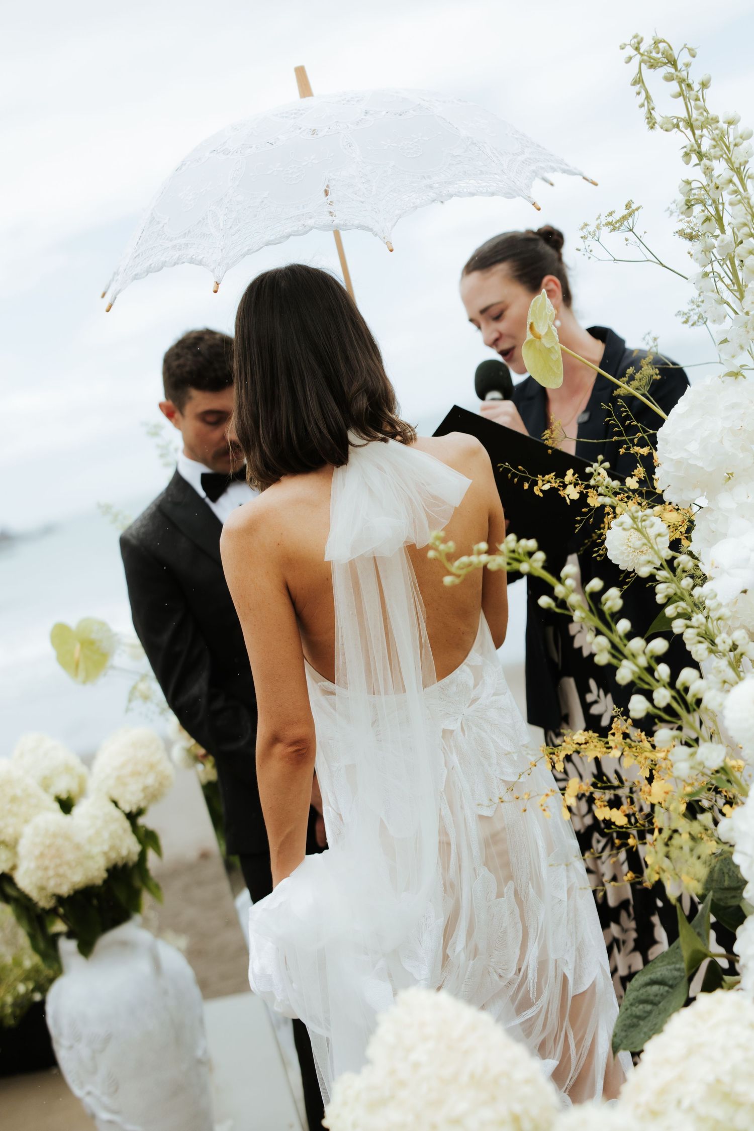 An outdoor wedding ceremony with white floral decorations and a lace parasol.