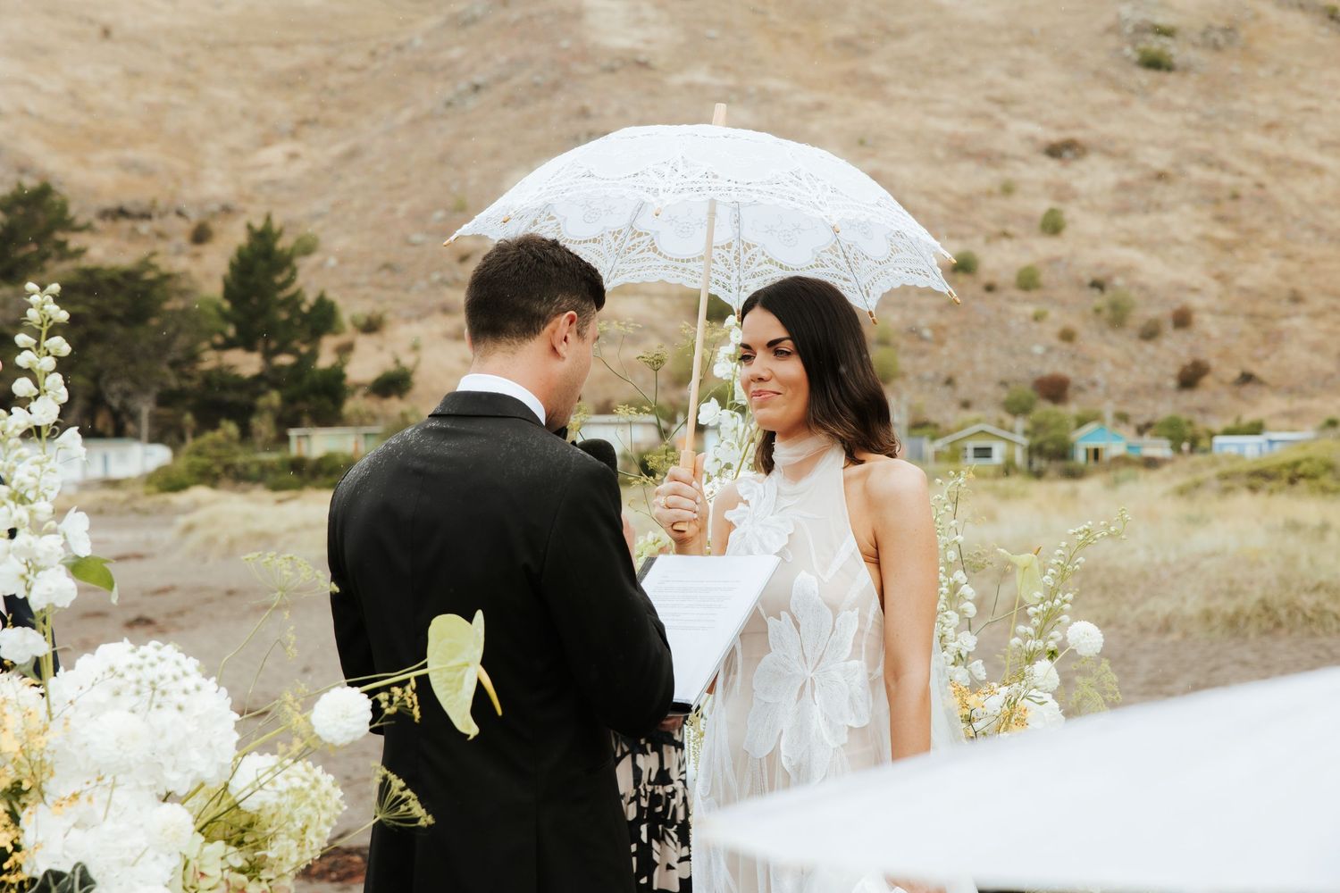 Couple shares intimate moment during outdoor wedding ceremony against mountain backdrop.