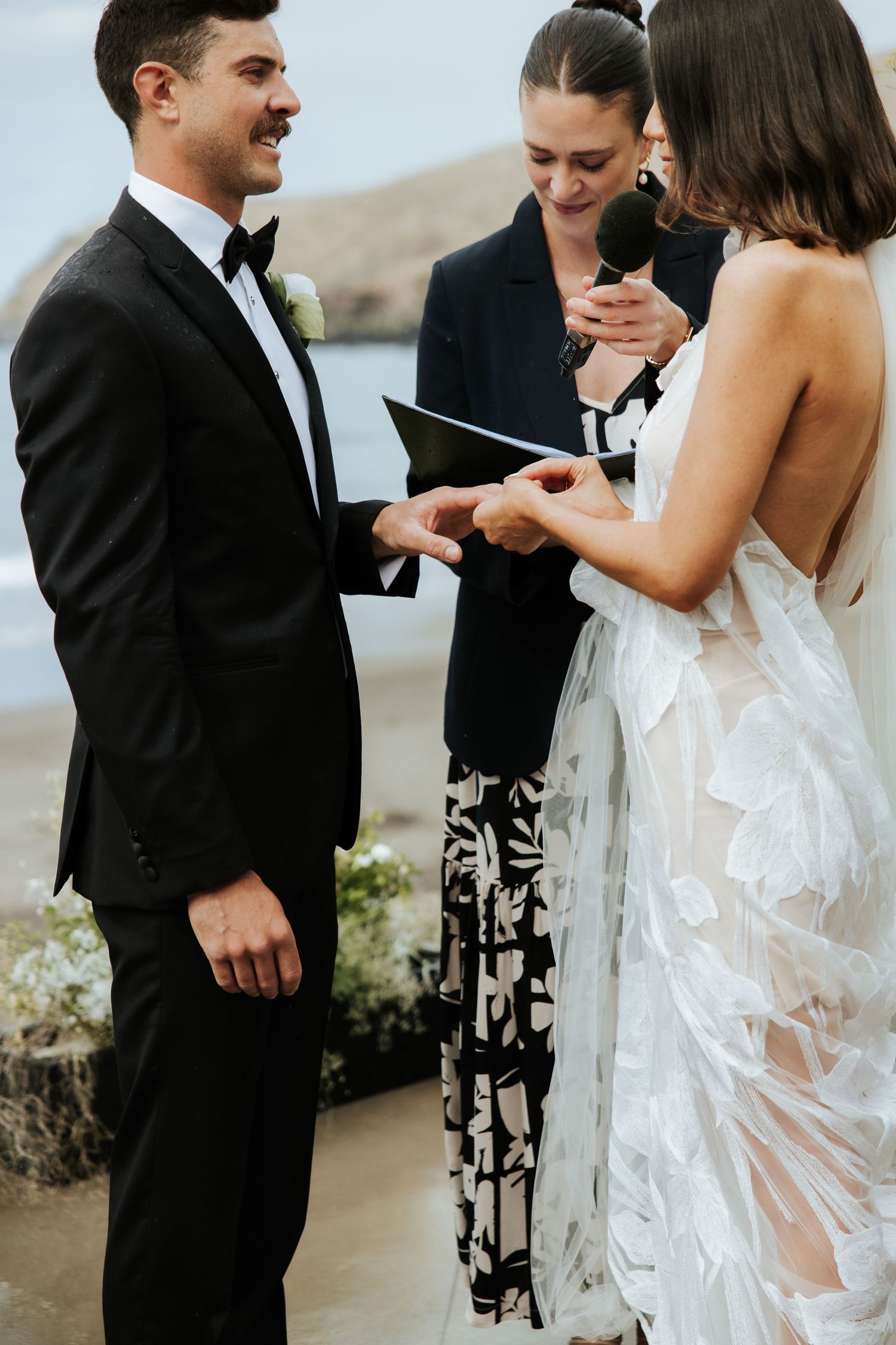 An outdoor wedding ceremony with stunning coastal views as a couple exchanges rings.