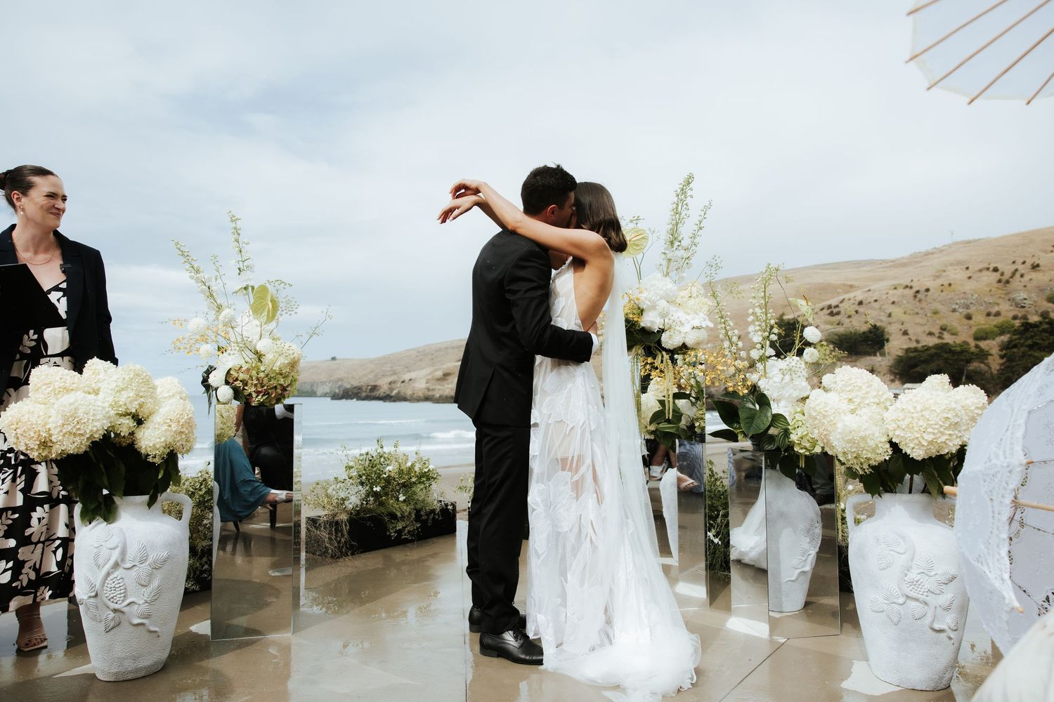 Elegant white floral arrangements line an outdoor wedding ceremony space with coastal views.