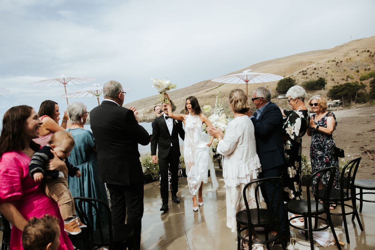 Wedding guests celebrating outdoors with raised glasses against a desert mountain backdrop.