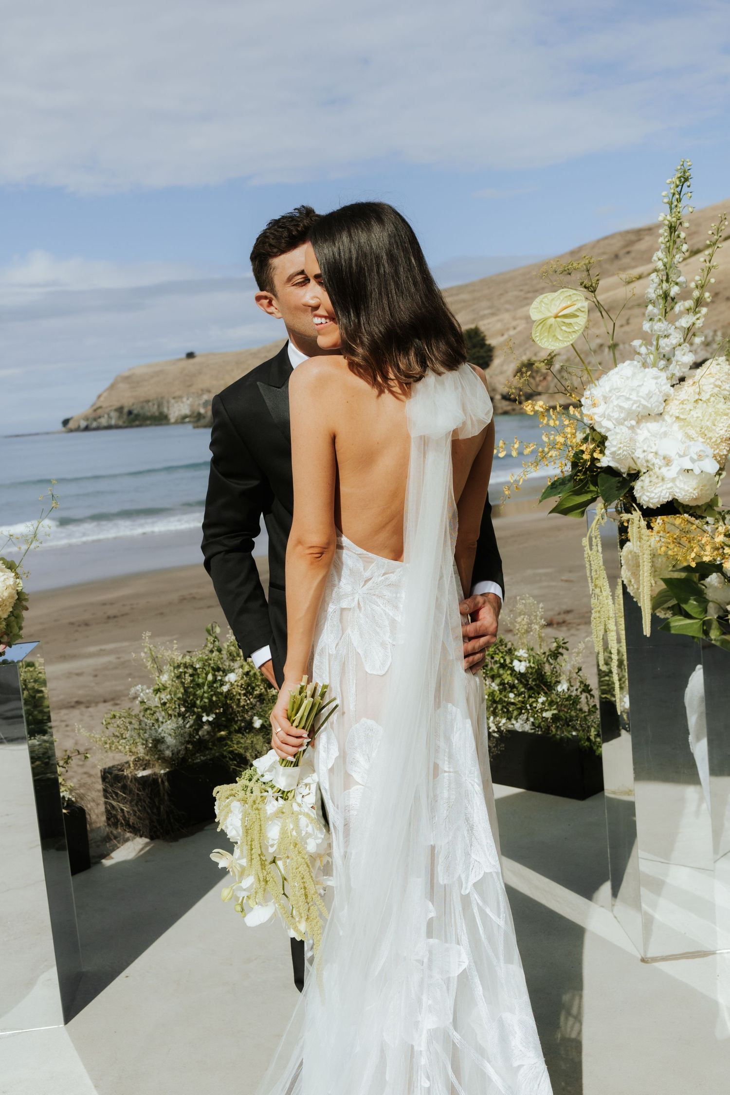 Modern beach wedding ceremony setup with white floral arrangements and ocean backdrop.