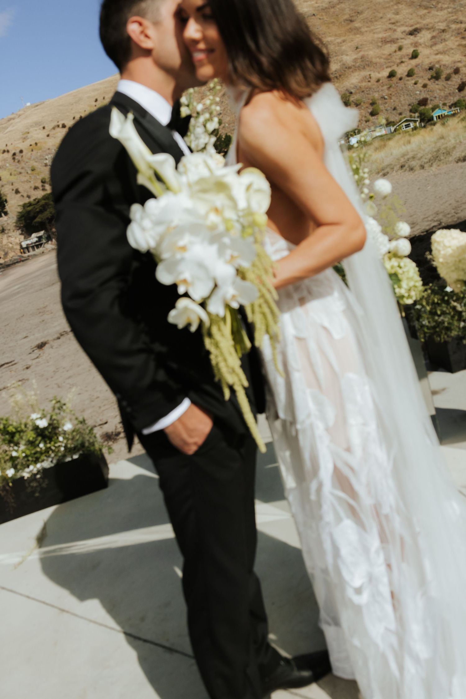 Newlyweds share an intimate moment in front of a desert backdrop with white orchid bouquet.