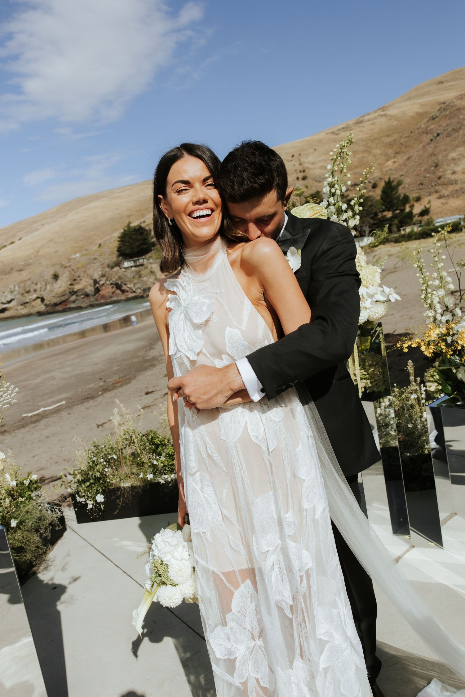 Newlywed couple shares joyful embrace during outdoor wedding celebration.
