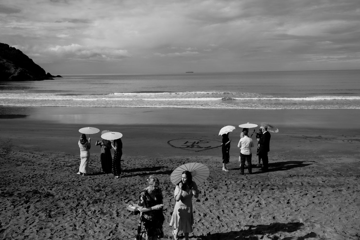 Black and white photo of beachgoers with umbrellas gathered on a scenic coastline.