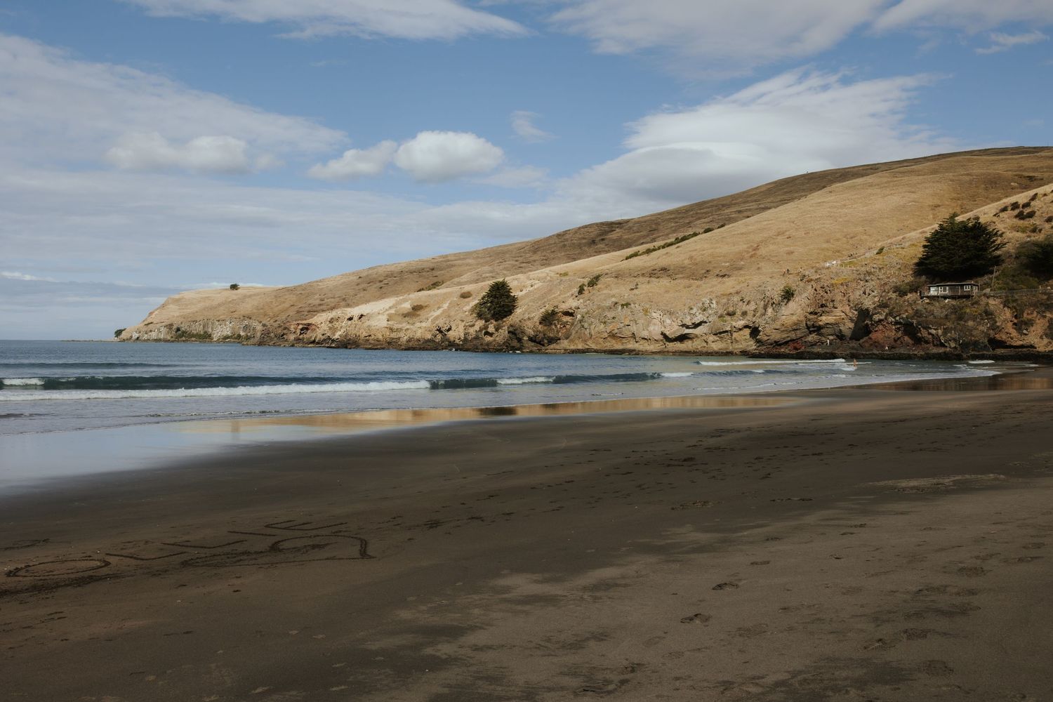 A serene coastal landscape with rolling hills and a sandy beach under blue skies.
