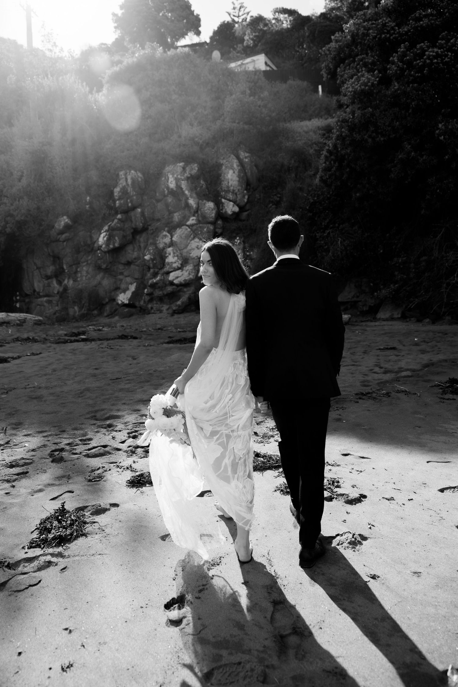 Silhouetted couple walking along a dramatic beach coastline at sunset.