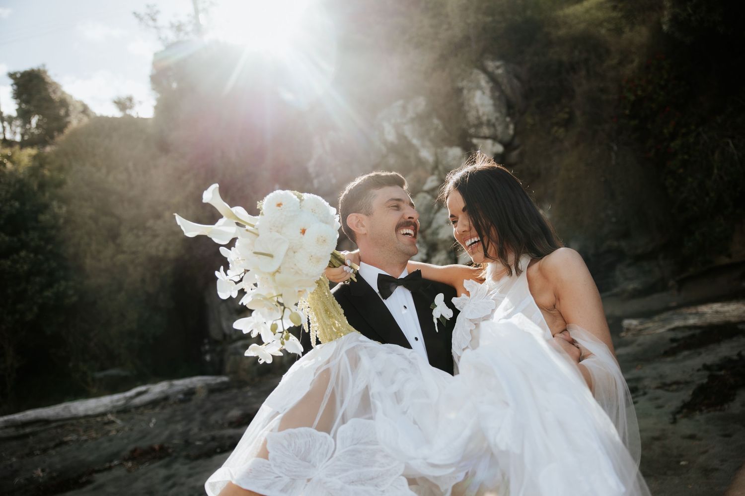 Ethereal beach wedding photos with flowing white dress catching sunlight through trees.