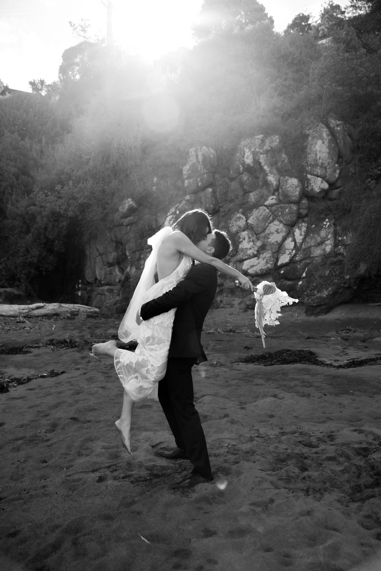 Dramatic black and white dance poses on a beach with rocky cliffs in background.