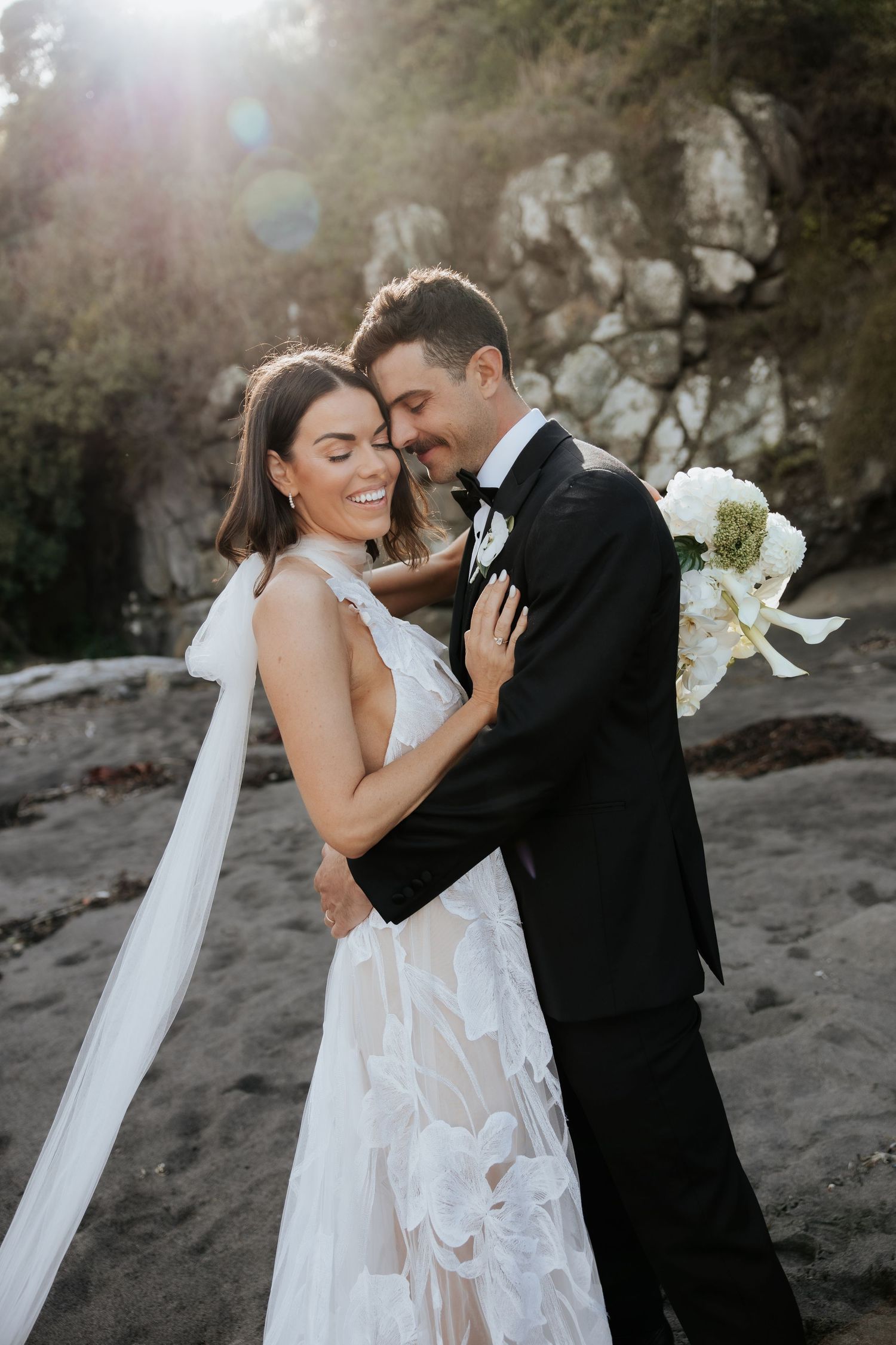 A romantic moment captured between newlyweds against rocky cliffs at sunset.