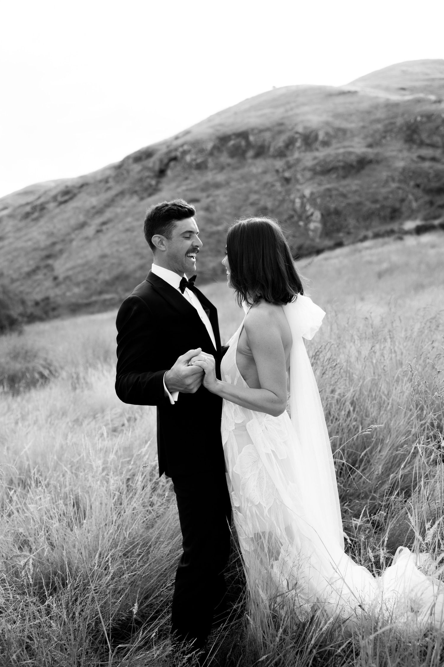 Black and white wedding portraits show couple embracing on a scenic hillside.