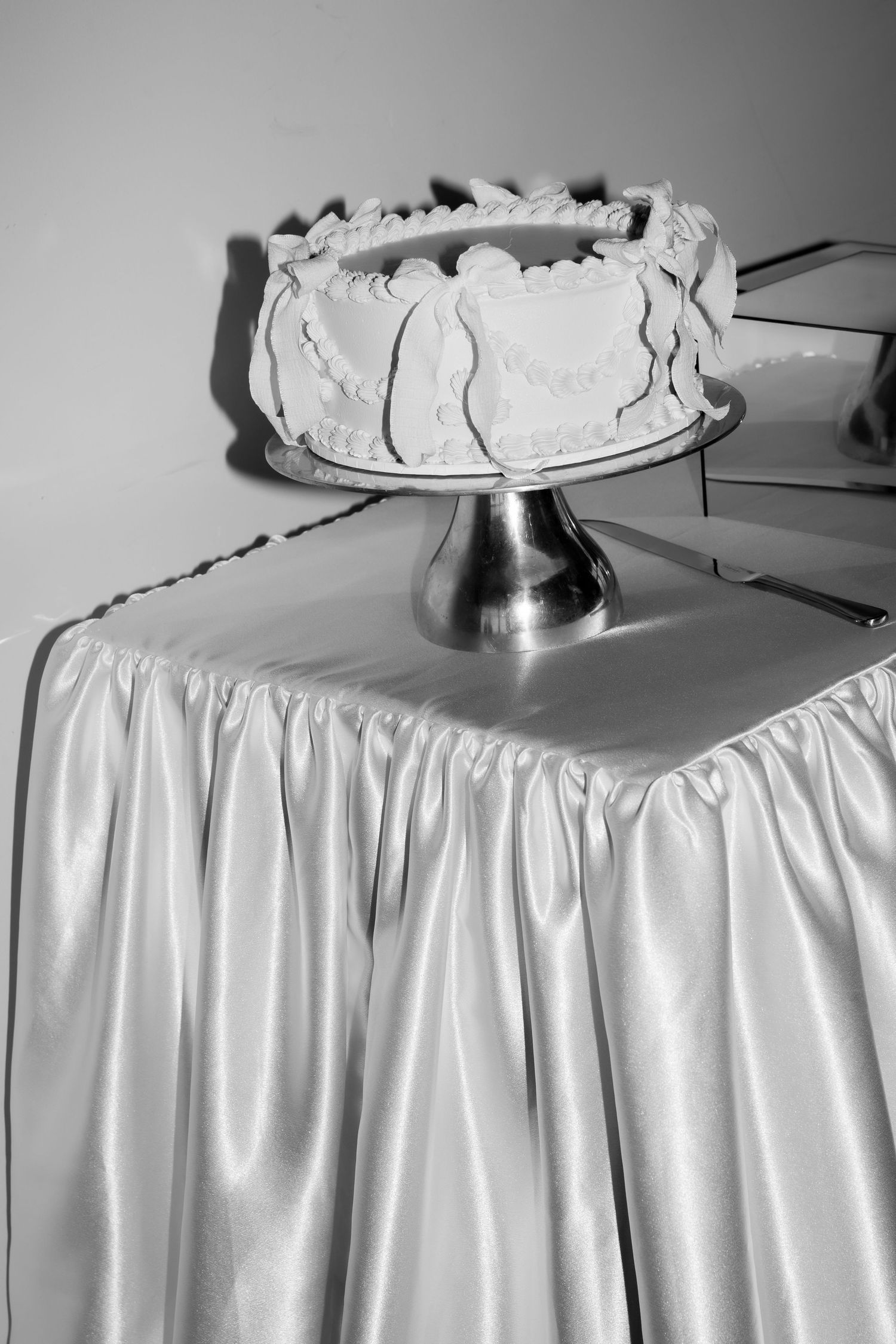 White frosted wedding cake displayed on a silver cake stand with satin tablecloth.