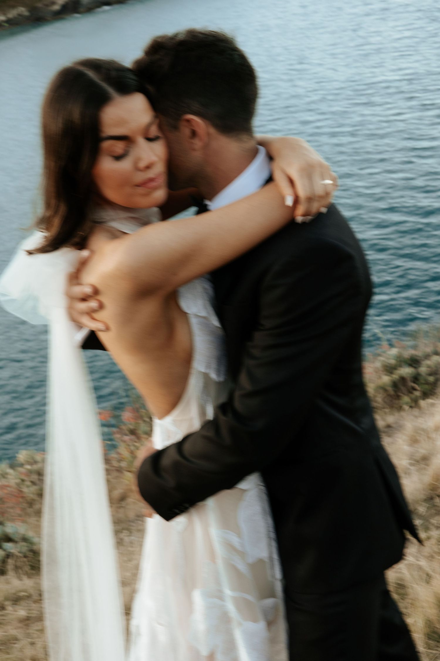 A tender moment between newlyweds embracing by the ocean during their coastal wedding photoshoot.