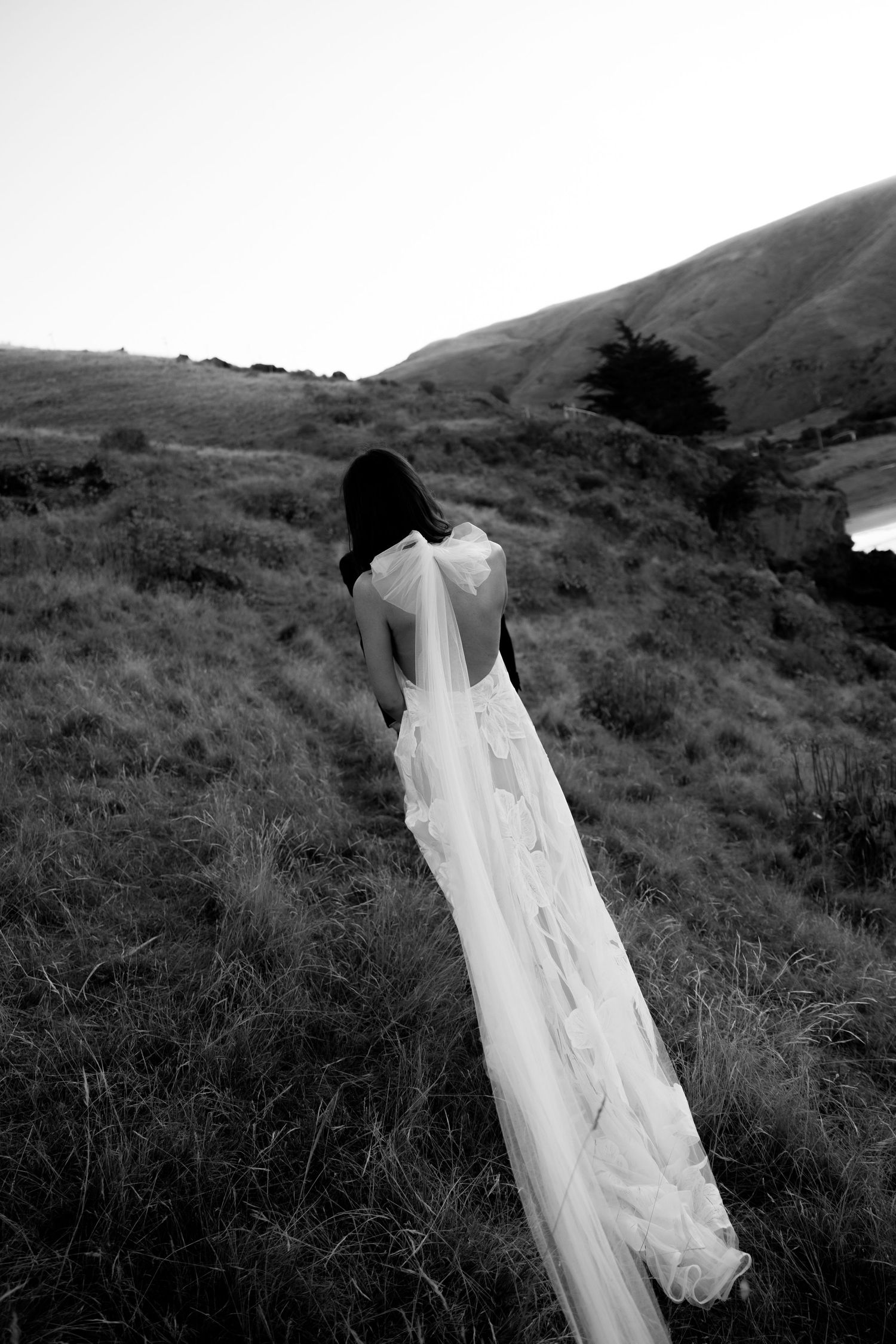 A flowing white wedding dress photographed against rolling hills in black and white.