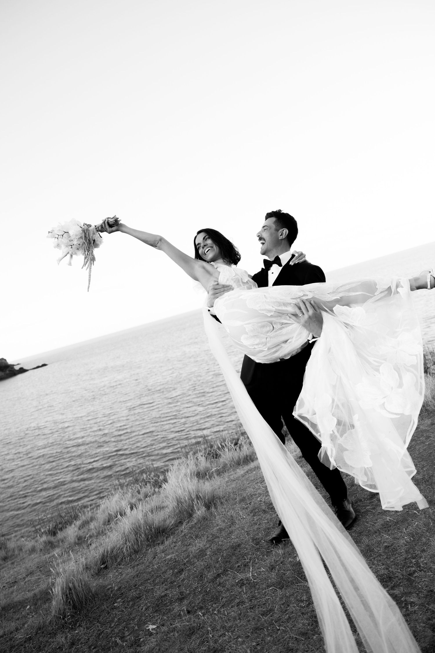 A couple dances dramatically on a beach as the bride's white dress and veil flow in the wind.