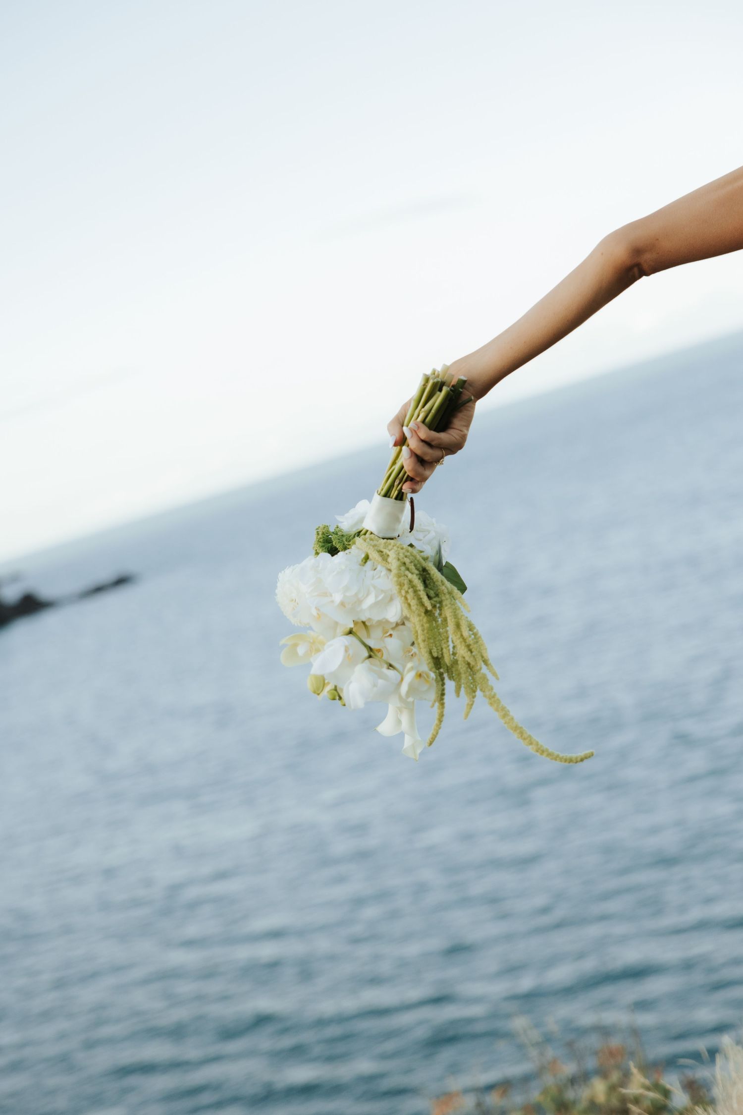 An arm holds white flowers over the ocean horizon.