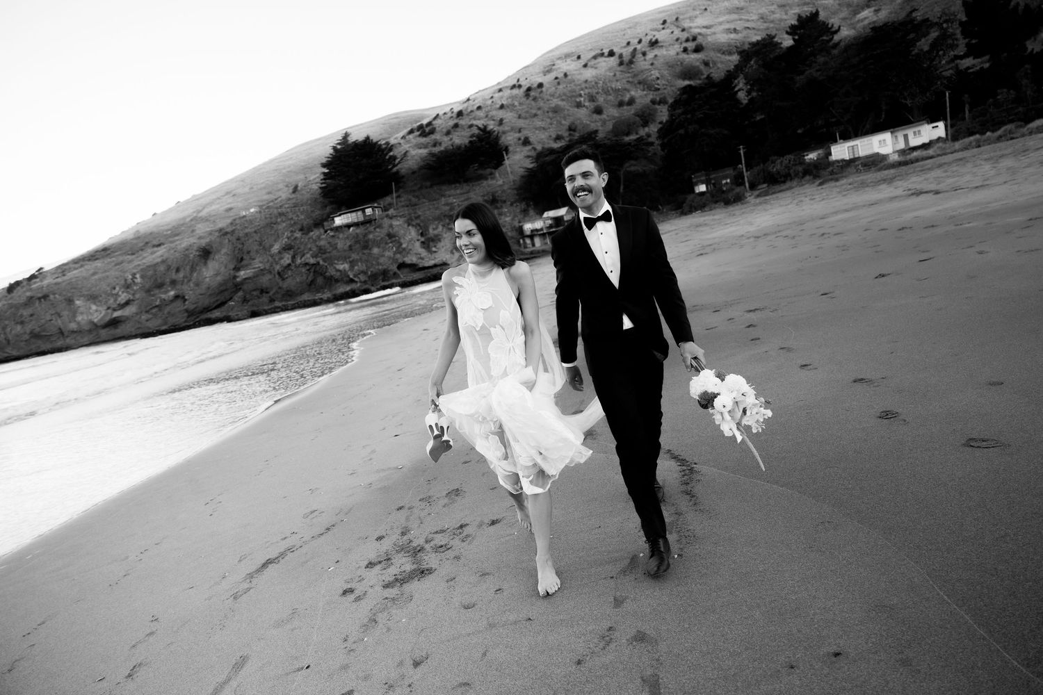 Black and white photos of a couple walking along a scenic beach on their wedding day.