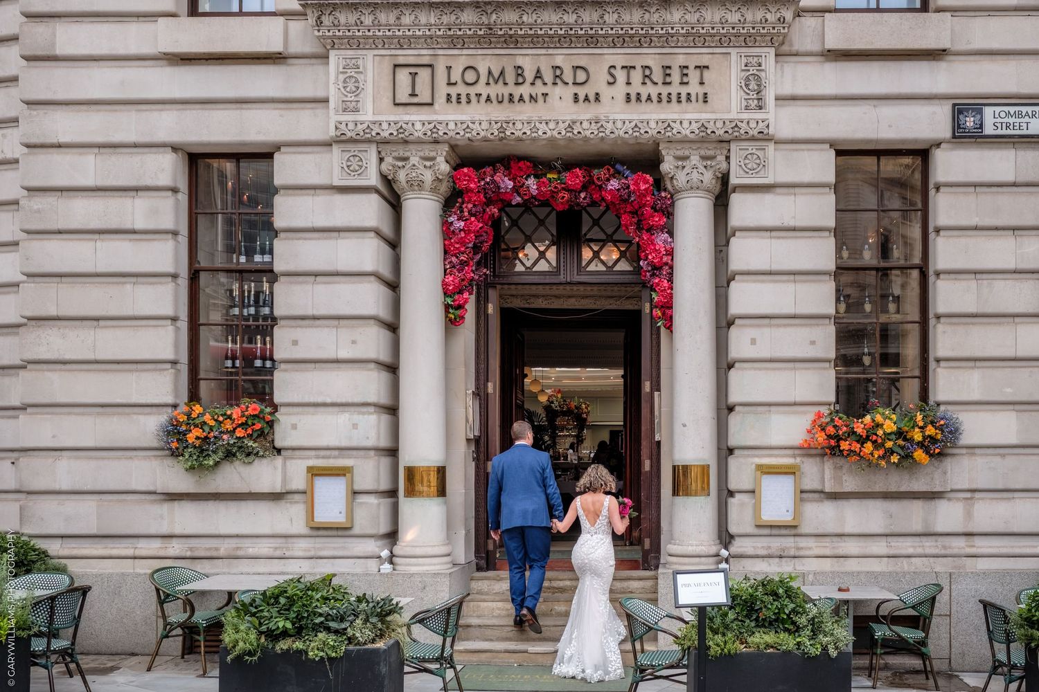 Wedding couple entering Lombard Street building decorated with red floral arch.