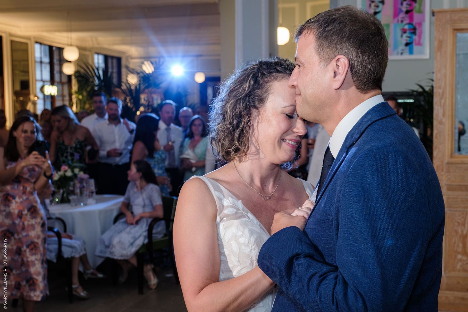 A romantic first dance moment between newlyweds at their wedding reception as guests look on from their tables.