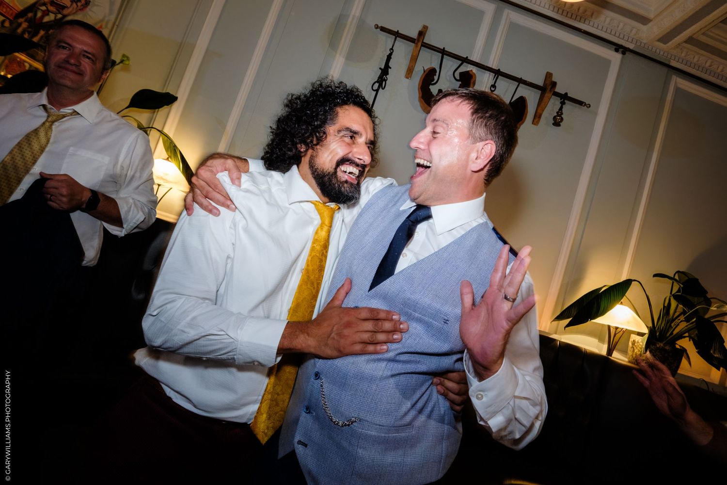 Two joyful party guests sharing a laugh and embracing during a celebratory indoor event.