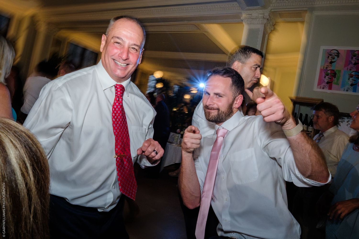 People dancing and celebrating at a formal event in white dress shirts and red ties, having fun at what appears to be a party.