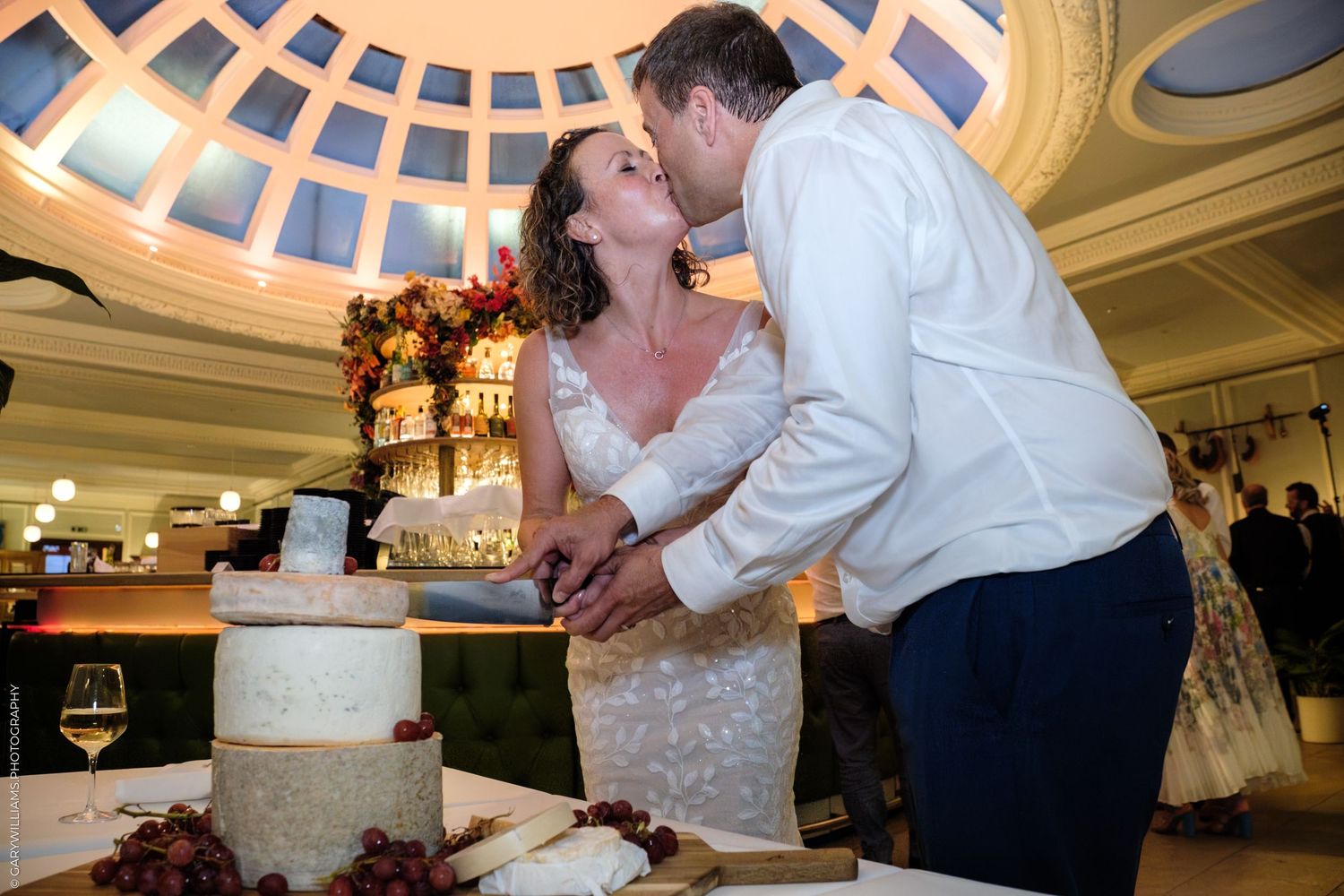A couple shares a romantic kiss during their wedding reception underneath elegant ballroom lighting.