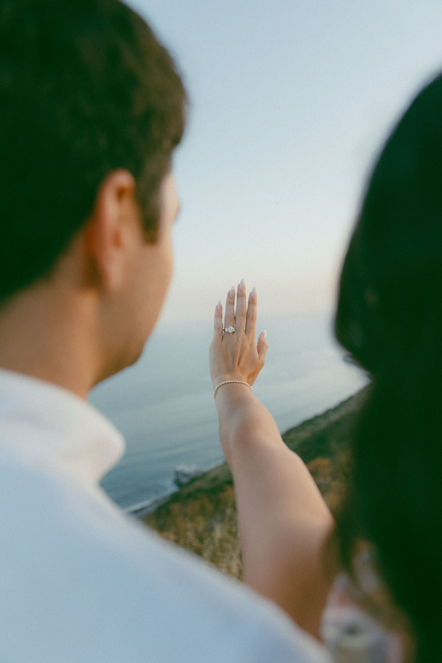 A close-up view of an engagement ring being shown against an ocean backdrop during a romantic sunset moment.