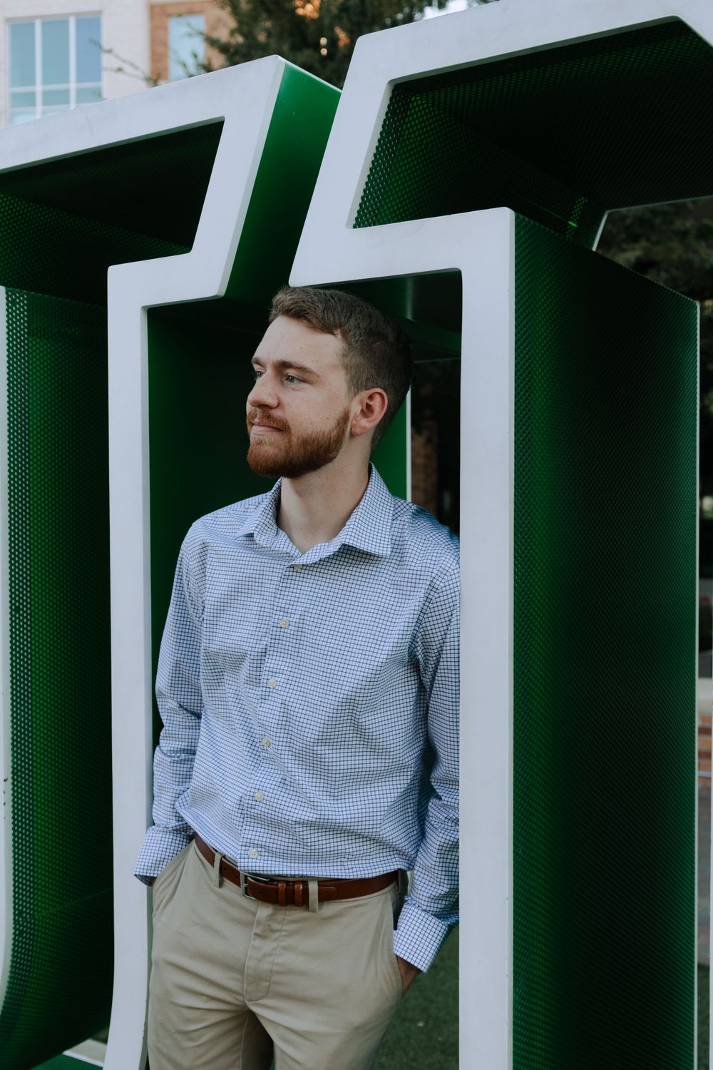 A graduate stands in a green and white architectural frame wearing business casual attire.