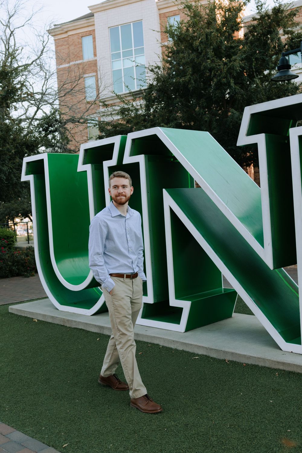 Large green and white university letters displayed on campus lawn with brick building in background.