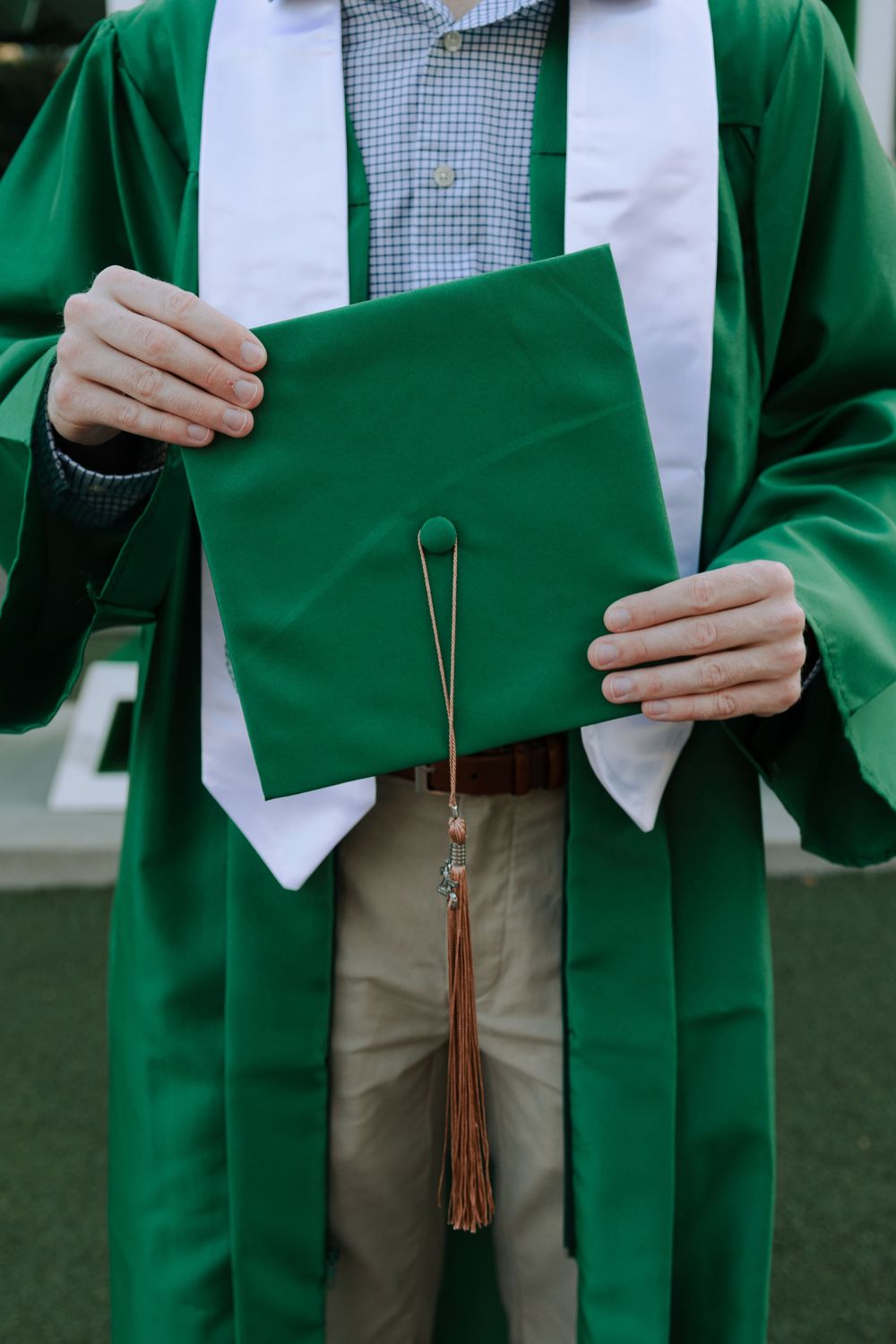 Close-up shots of a graduation gown in emerald green with white stole and tassel details.