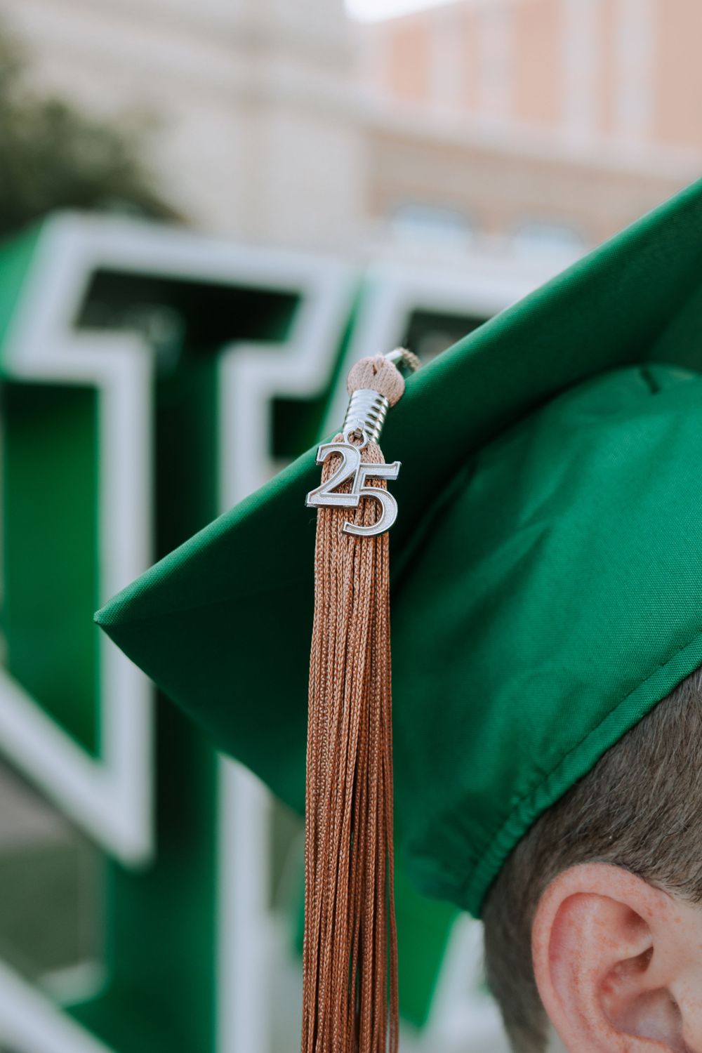Graduation caps with gold tassels shown in a row against an emerald green background at commencement ceremony.