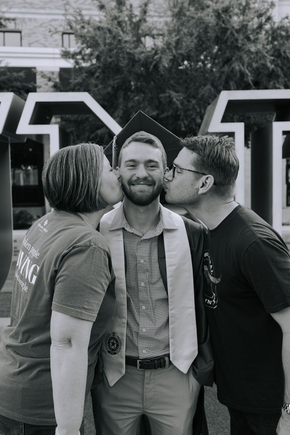 A graduation celebration moment captured in black and white as two people kiss a graduate on the cheeks.