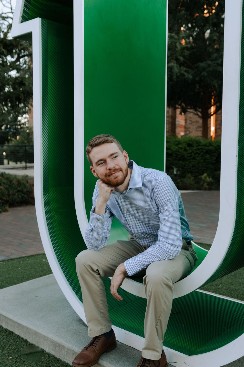 A person sits thoughtfully on a large green and white decorative letter U sculpture on a university campus.