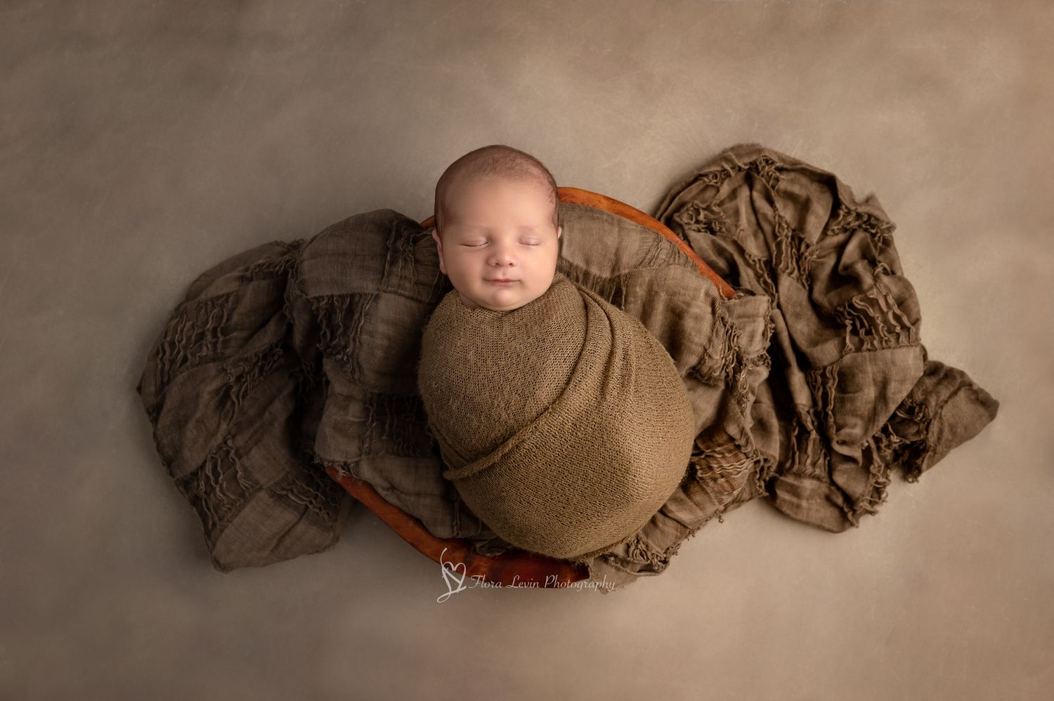 A sleeping newborn wrapped in brown swaddle blankets in various curled positions against a neutral backdrop.