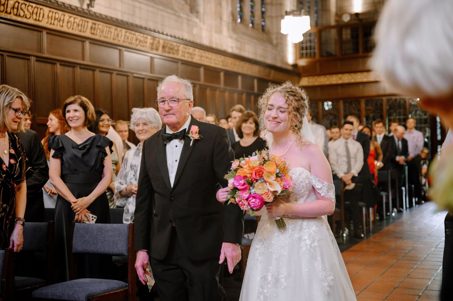 Elegant church wedding ceremony with guests seated in wooden pews and floral decor along the aisle.