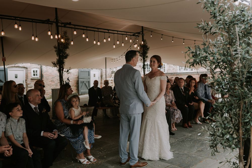 Wedding ceremony under a tent at The Old Cow Shed with greenery and string lights creating a warm, romantic ambiance – Melton Mowbray.