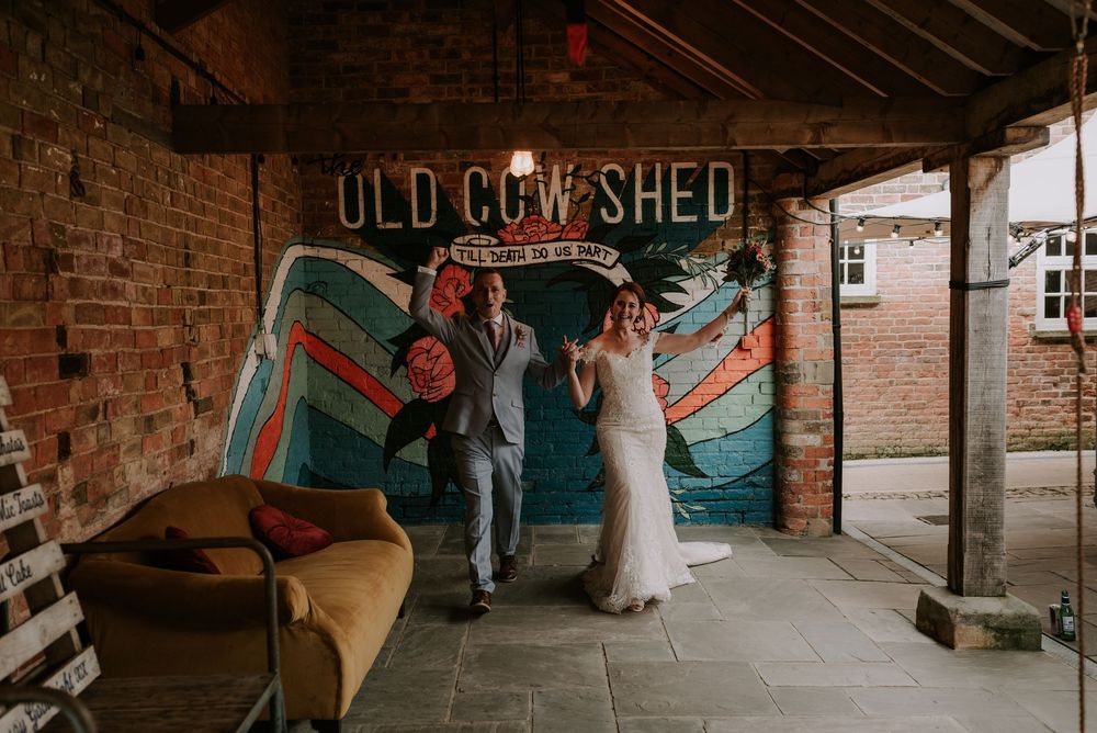 ouple walking toward camera with arms raised at rustic wedding with vintage decor and exposed brick – Old Cow Shed, Melton Mowbray