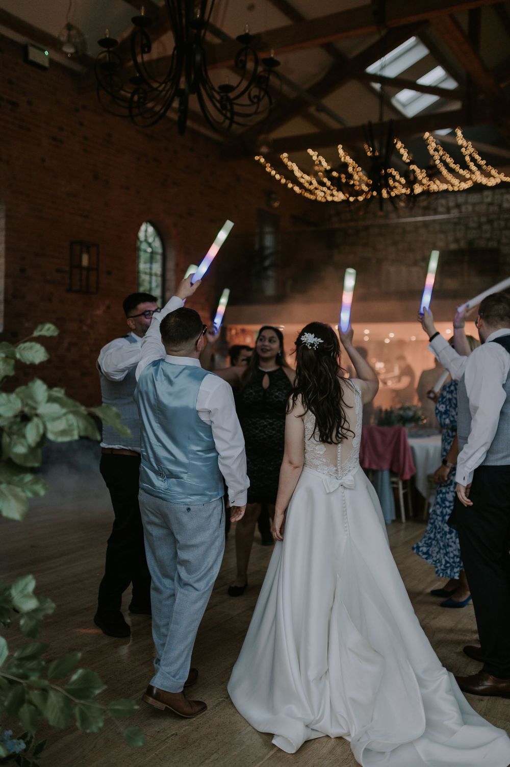 Wedding guests dancing with LED foam sticks under string lights, backs to camera at The Carriage Hall wedding