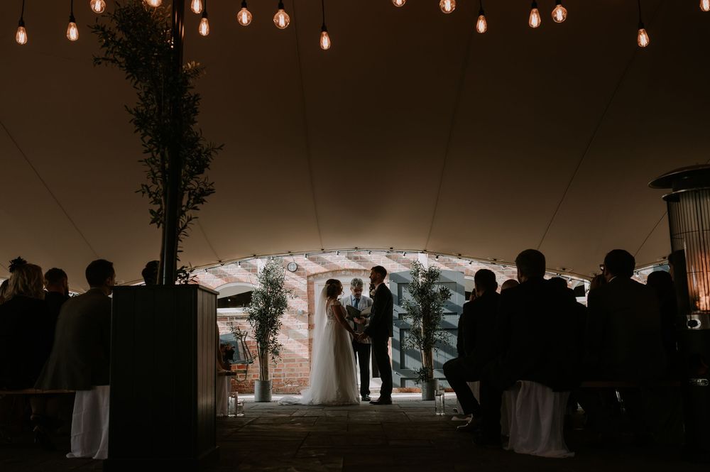 Dimly lit wedding ceremony under canopy with string lights and warm ambiance, guests silhouetted – Old Cow Shed, Melton Mowbray wedding