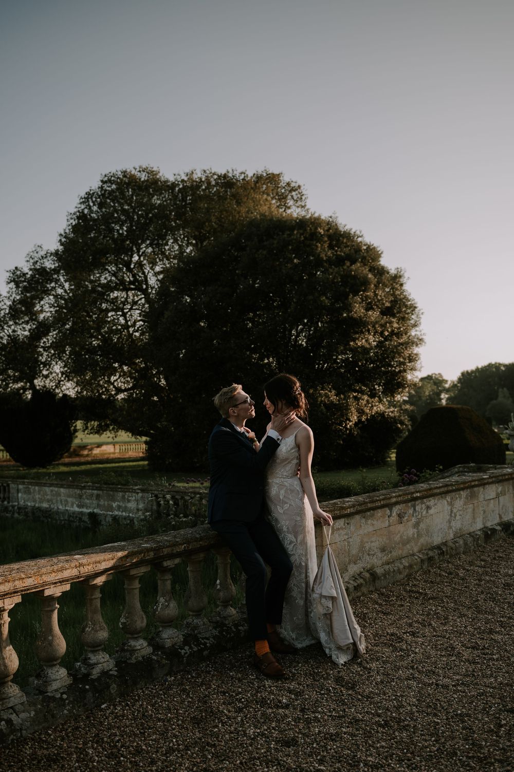 Couple leaning against historic stone wall at sunset, groom perched and bride leaning into him – Prestwold Hall, Loughborough wedding.