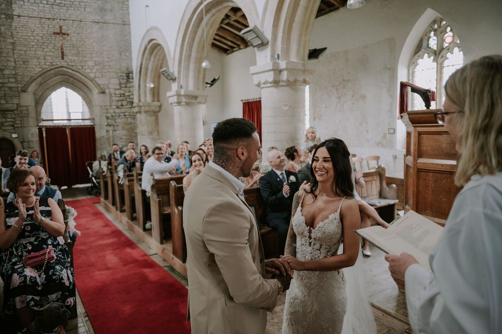 Bride and groom holding hands during wedding ceremony in historic church with stone arches and red carpet – Melton Mowbray wedding.