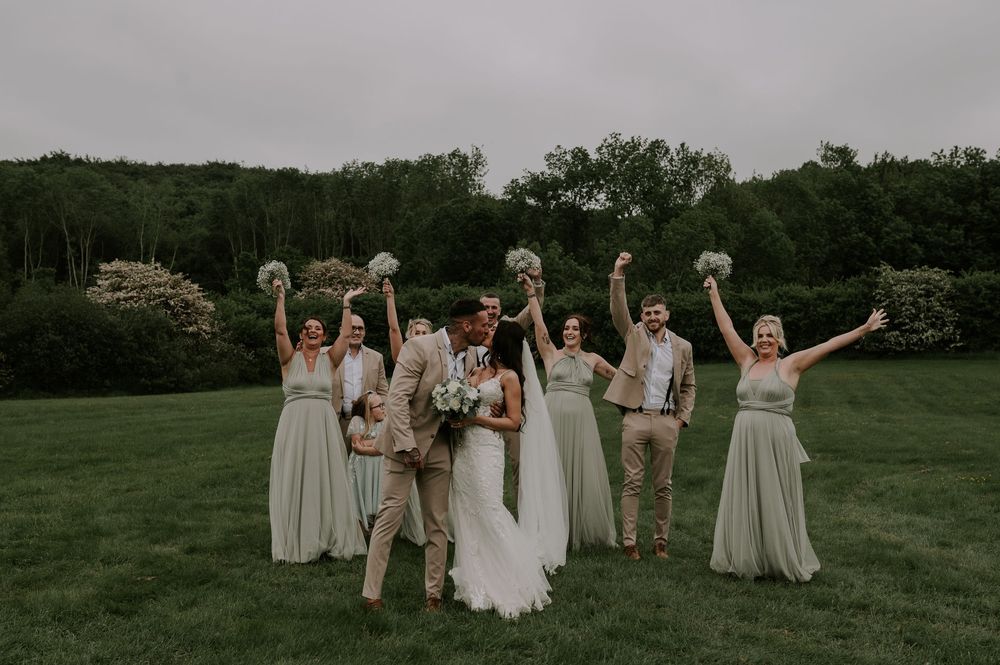 Wedding party celebrating with raised arms in green field outdoors – Chequers Inn, Grantham wedding