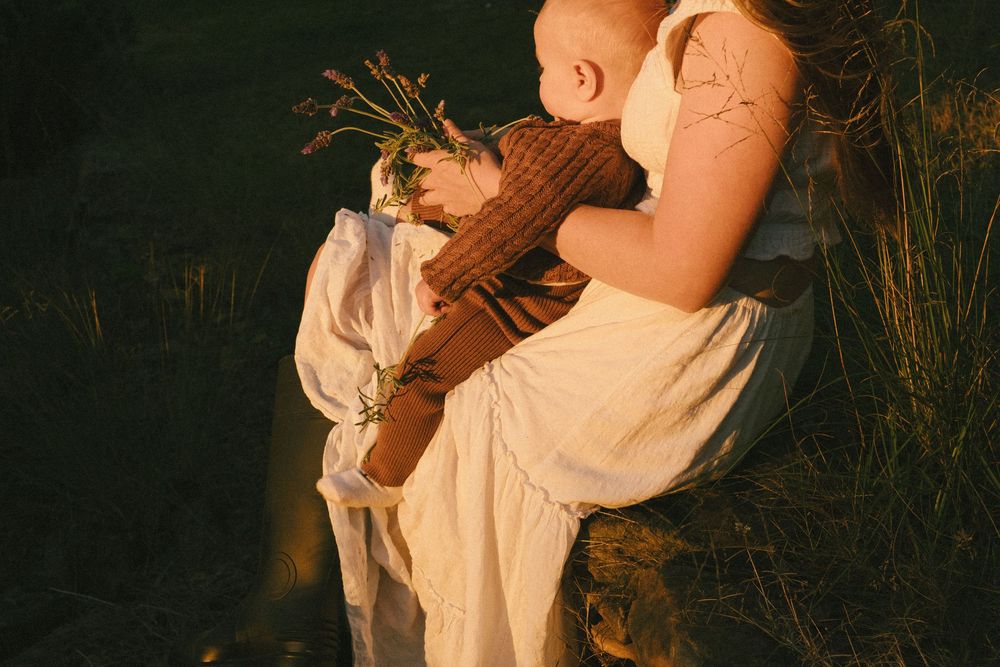 Side view of parent holding baby in brown outfit against dark background at sunset.